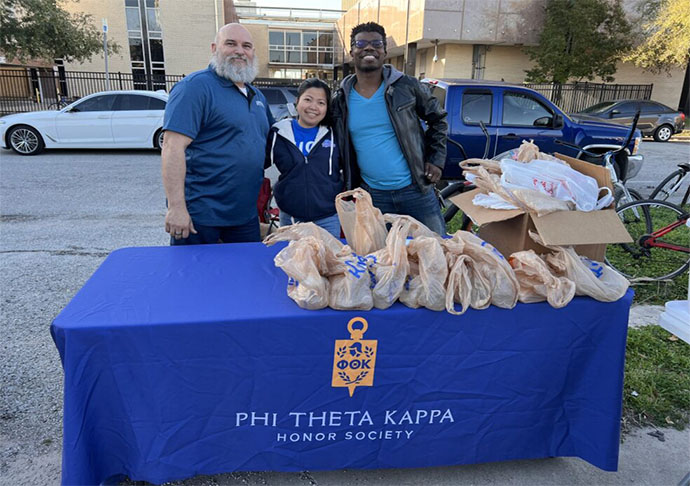 Three people stand at table with bags of food ready to donate