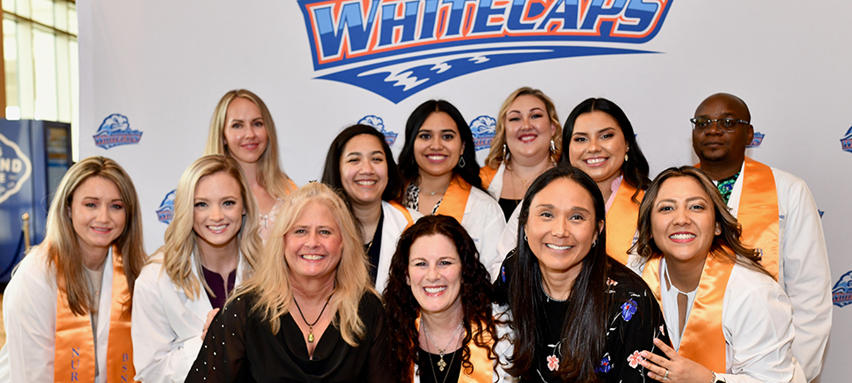 2023 BSN grads, director and instructor, smiling in front of a Whitecaps backdrop